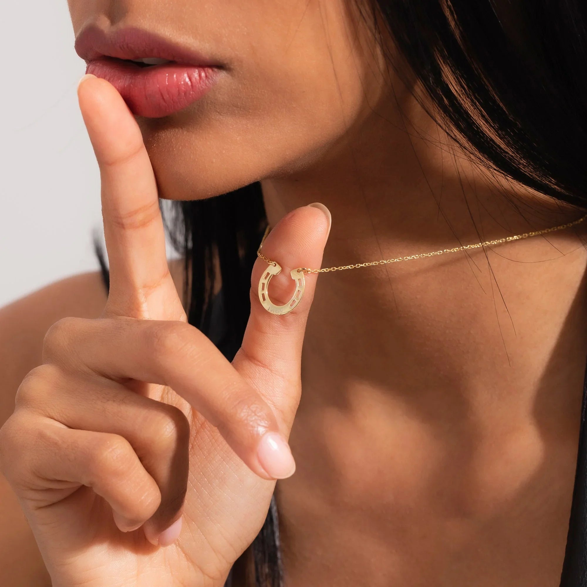 A woman wearing a delicate gold personalized horseshoe necklace paired with a black leather jacket